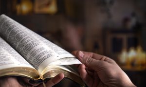Man's hands over the Bible, against the background of the living room.