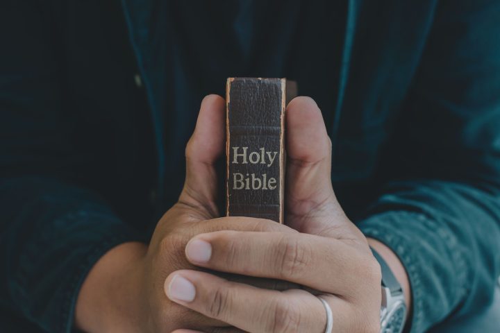 A Man praying holding a Holy Bible and praying in bed room.
